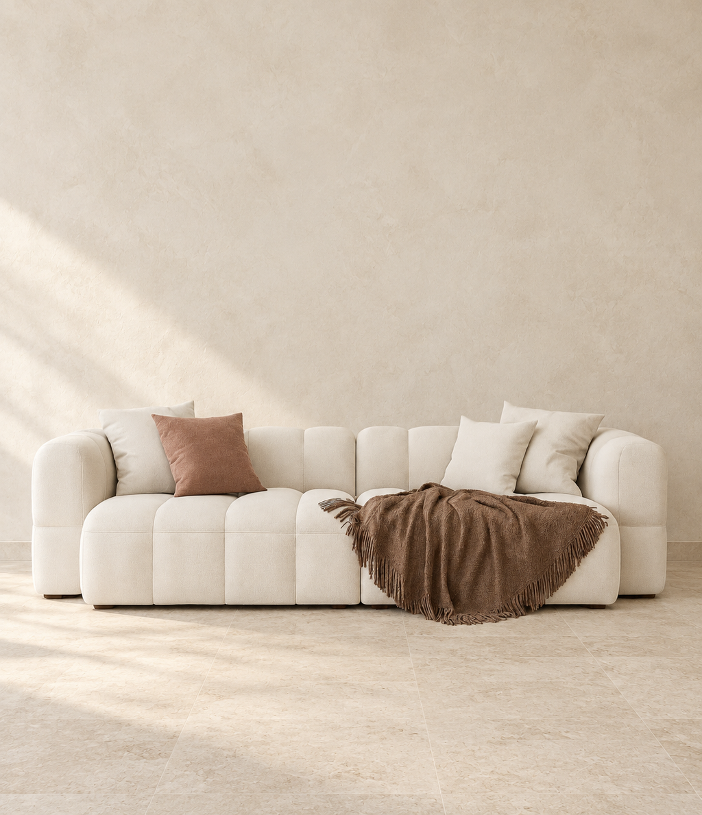 AI-assisted styled view of the Kravi sofa, showing pale-toned segmented upholstery, cushions and a brown throw for visual reference.